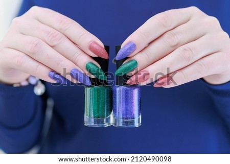 beautiful Woman's hands with long nails and multi-colored manicure, bottles of nail polishes