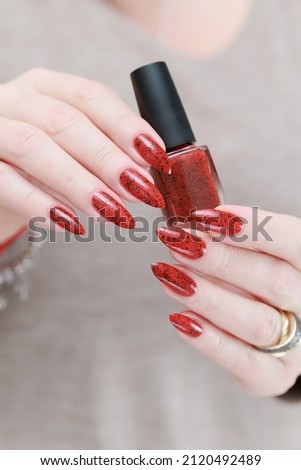 beautiful Female hand with long nails and a bright red manicure holds a bottle of nail polish