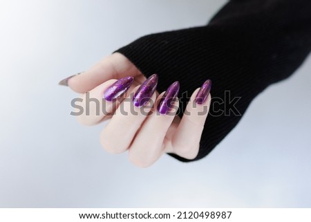 beautiful Female hand with long nails and purple plum manicure holds a bottle of nail polish