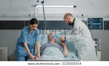 Sick woman hyperventilating and asking about medical assistance while doctor and nurse rushing to help with respiratory problem. Specialists using oxygen tube and oximeter for patient Royalty-Free Stock Photo #2120505014