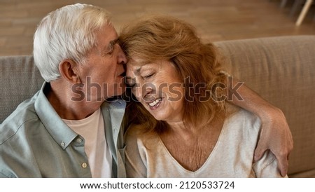 Partial image of senior caucasian couple sitting and resting on sofa at home. Man hugging and kissing his happy wife. Concept of family relationship and closeness. Idea of domestic lifestyle. Daytime
