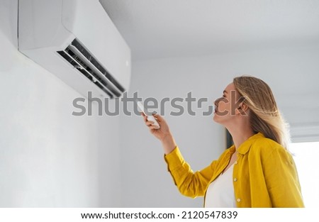 Woman holding remote control aimed at the air conditioner. Royalty-Free Stock Photo #2120547839