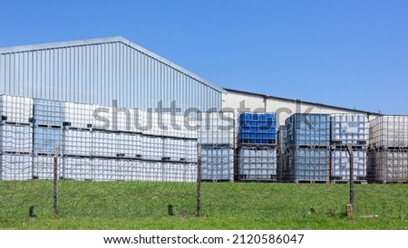 Industrial chemical metal caged holding plastic tanks for transporting liquids stacked outdoors factory yard.