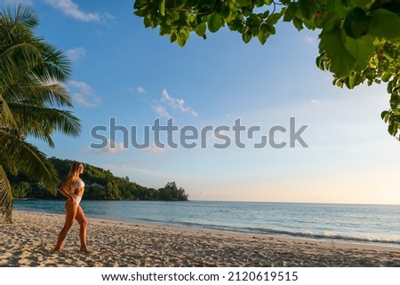 Young attractive blonde girl near palm at wild beach at summer vacation