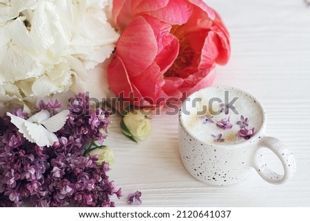 Beautiful peony, lilac, roses flowers arrangement with stylish cup of coffee. Happy mothers day. Good morning. Delicious coffee with lilac petals and stylish bouquet on white wooden background