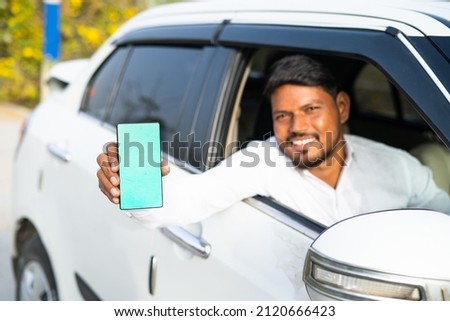 Foucs on mobile, cab driver showing mobile phone with green screen mockup by looking at camera - concept of online booking servive, app advertising for travel service and promotions Royalty-Free Stock Photo #2120666423