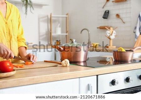 Cookware and woman slicing carrots on wooden board in kitchen Royalty-Free Stock Photo #2120671886