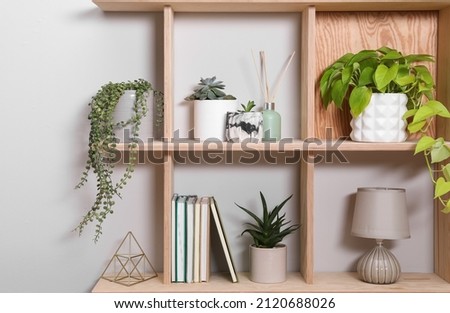 Wooden shelving unit with interior accessories and houseplants on white wall Royalty-Free Stock Photo #2120688026