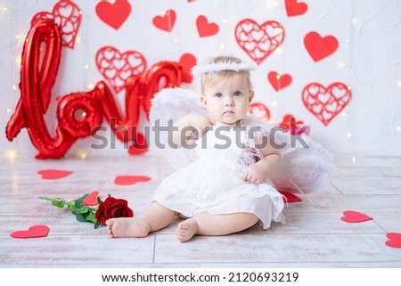 a cute little girl in an angel costume with wings on a background of red hearts and the inscription love. the concept of valentine's day, valentine's day