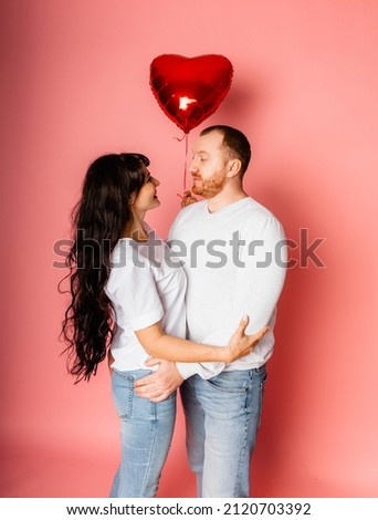 a man and a woman on a pink background hold a large inflatable red heart-shaped balloon in their hands. Holiday concept - Valentine's Day