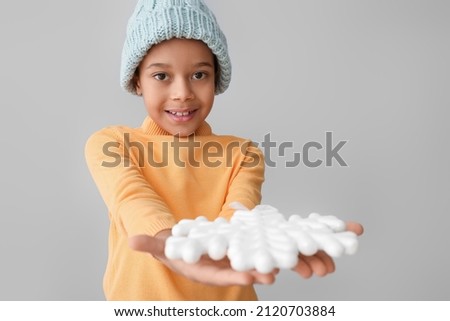 Cute little African-American boy in winter clothes and with snowflake on grey background
