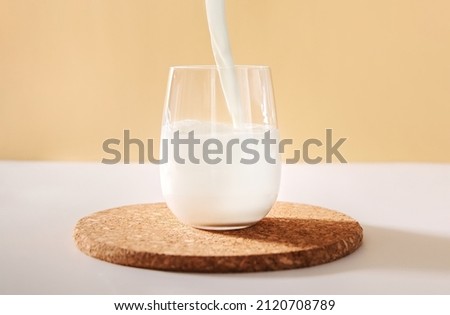 Pouring milk in glass on a light neutral background. Royalty-Free Stock Photo #2120708789