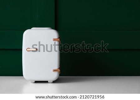 Small cosmetic refrigerator on table near green wall
