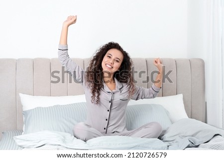 Happy beautiful African American woman stretching on bed at home