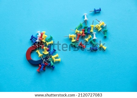 Horseshoe magnet holding a bunch of colorful pins on a blue background.