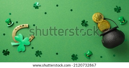 Top view photo of the bronze horseshoe and a lot of confetti in shape of clovers dots hats and black pot with coins on the green isolated background blank space