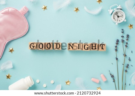 Top view photo of wooden cubes good night text lavender white alarm clock pink silk sleeping mask earplugs open bottle with pills feathers and golden stars on isolated pastel blue background
