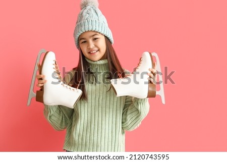 Little Asian girl in warm clothes with ice skates on pink background