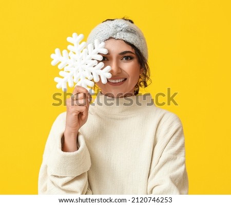Beautiful smiling woman holding big snowflake on yellow background