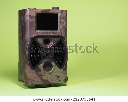 Trail camera on a green background. Photo and video trap. Animal and surroundings monitoring device with motion sensor and night vision