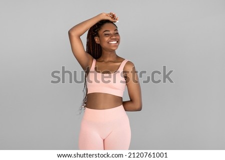 Portrait of happy young black woman in sports outfit posing and smiling on grey studio background. Fit millennial African American female being in great shape, leading active lifestyle Royalty-Free Stock Photo #2120761001