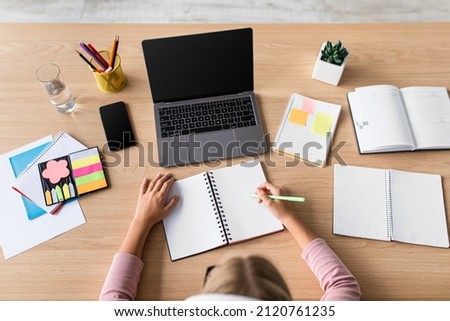 Blonde european teenage girl pupil study at home with computer with blank screen at table in kitchen, top view. Planning, knowledge, education, online lesson and new normal in covid-19 quarantine Royalty-Free Stock Photo #2120761235
