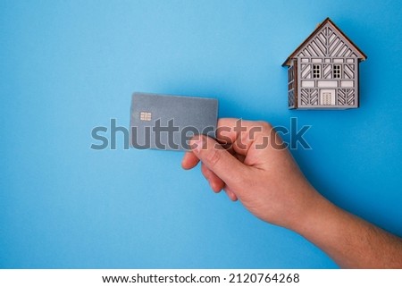 Wooden house on blue background. A man's hand holds a credit card. Business concept of Real Estate. Home Property for Sale and rent - copy space. Construction 