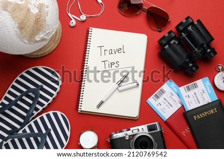 Flat lay composition with phrase Travel Tips written in notebook, passports, tickets and binoculars on red background