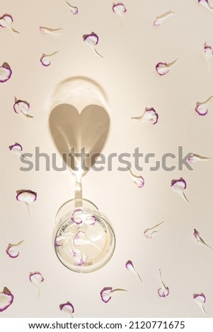 Flower petals and glass of vine with heart shade against pastel beige background. Romantic love scene. Flat lay patern.