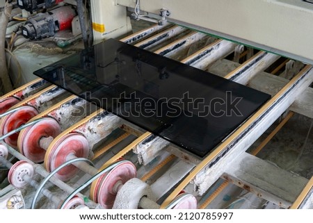 Glass processing and polishing. Dark glass on the conveyor of a glass polishing machine. Royalty-Free Stock Photo #2120785997