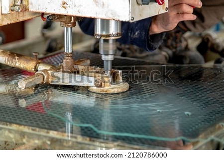 Glass processing. Drilling machine for making holes in tempered glass. The cutter makes a hole in the glass. Royalty-Free Stock Photo #2120786000