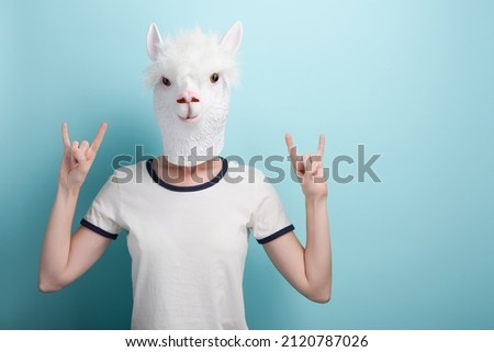 Woman in alpaca mask with hands in rock sign gesture, isolated on blue background