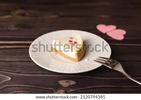 A plate with a piece of delicious cheesecake and pink hearts on a wooden table, close-up. Selective focus.