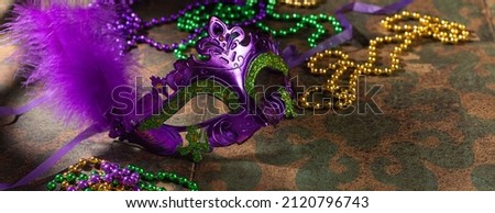 Colorful festive mardi gras or carnivale mask with green, violet and yellow beads on a rustic tile background, selective focus, copyspace, banner