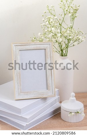 Portrait white picture frame mockup on wooden table. Modern ceramic vase with gypsophila. White wall background. Scandinavian interior. High quality photo