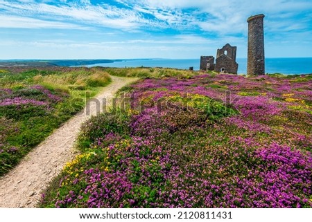 Relic of Cornish tin mining industry, on the clifftop of north Cornish coast in summertime, with UNESCO World Heritage status.Old brick chimney and ruins of shaft engine house against summer sky. Royalty-Free Stock Photo #2120811431