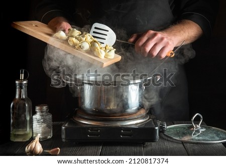 Professional chef cooks dumplings in a saucepan in the kitchen. Close-up of the hands of cook during work Royalty-Free Stock Photo #2120817374