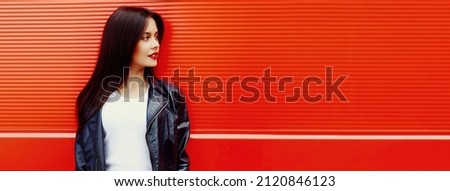 Fashionable portrait of beautiful young brunette woman model looking away in black leather jacket on red background, blank copy space for advertising text