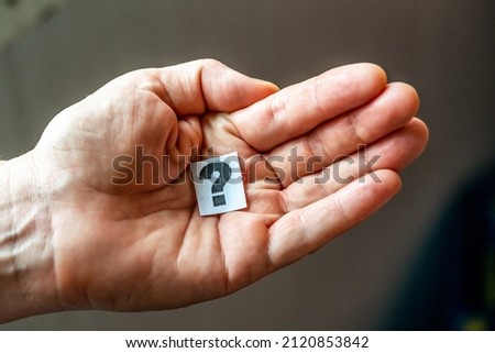 mans hand holds a sheet of paper with a question mark drawn on it