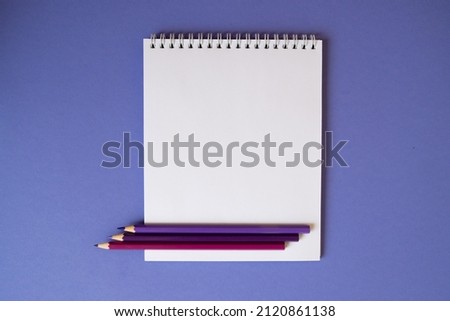 on a lilac background, a notebook with sheets of a spring for drawing, open on a blank page, three pencil lies on top