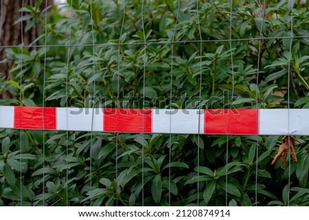 Closed area with brightly barricade with red and white tape wrapped on steel barrier with blurred green leaves in the park, Mobile steel fence while maintenance or repairing.