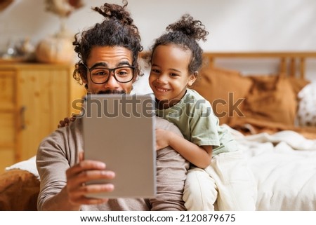 Happy african american family little boy son with young dad watching funny videos on tablet together at home, father with child using computer in bedroom while enjoying weekend