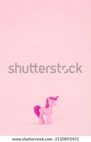 A toy pink unicorn with a pink hair and tail on a pink background. Poster for children's birthday. A minimal concept of fairy tales and magic.
