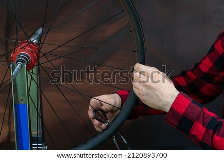 A bicycle mechanic in a red plaid shirt is assembling a wheel using a professional truing stand on a black background. Bicycle repair. The mechanic's face and hands are close-up while working.
