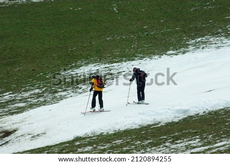 Two skiers putting on skis at the bottom of a ski slope finishng in the green valley, covered with artificial snow due to warm winter. Bottom of the Ahorn mountain, Mayrhofen, Austria