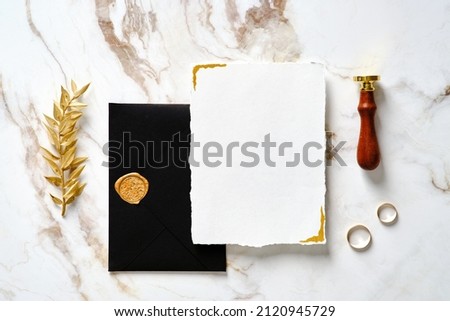 Elegant wedding stationery set. Wedding invitation card mockup, black wedding envelope with wax seal stamp, golden ring, golden branch on marble desk.