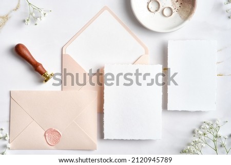 Wedding stationery set. Pastel pink wedding envelopes with wax seal stamp, wedding invitation card, golden rings on stone table. Flat lay, top view, copy space.