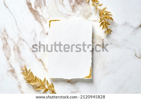 Blank paper card with golden floral branches on marble table. Wedding invitation mockup, birthday greeting card design.