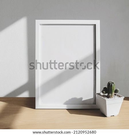 The blank white vertical frame. Decorative still life empty frame. Sunlight through the window on the table and wall interior. mockup design background.