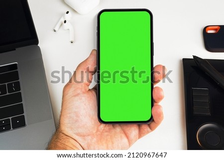 Man holding a smartphone with green screen on white background table. Office environment. Chroma Key.
